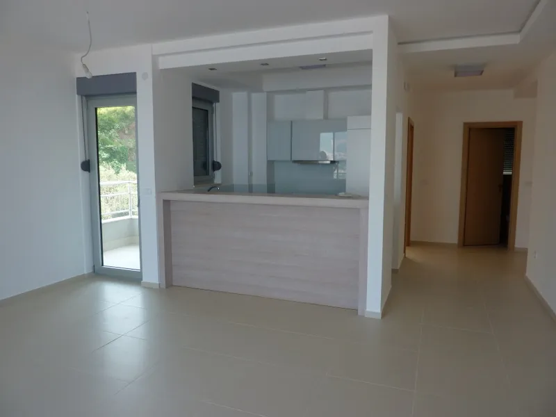 Living room with open kitchen, tiled floor, and balcony door.