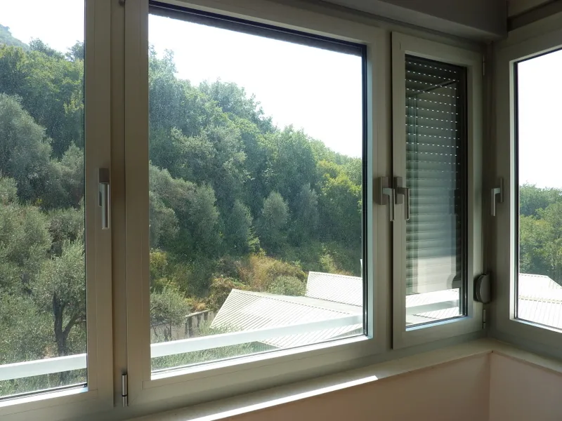 A window with white frame looking out at green trees and a house roof.
