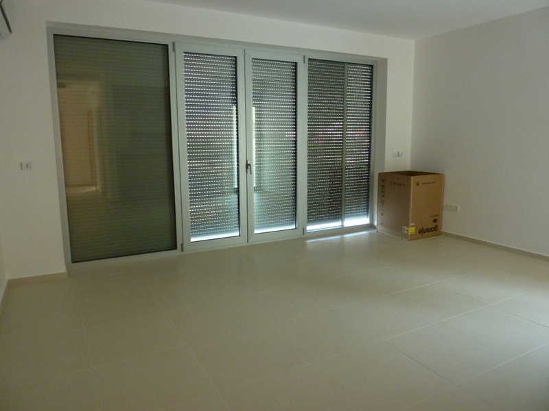 Svetao dnevni boravak sa panoramskim prozorima i roletnama u novom stanu u Pržnu, Crna Gora. Porcelanske pločice na podu.