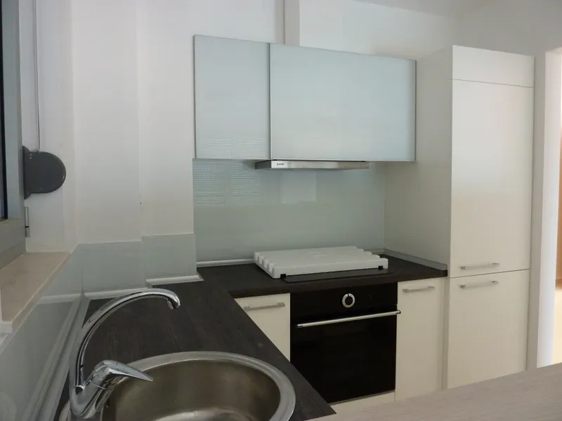 A modern kitchen interior with a sink, stove, oven, and white cabinets.