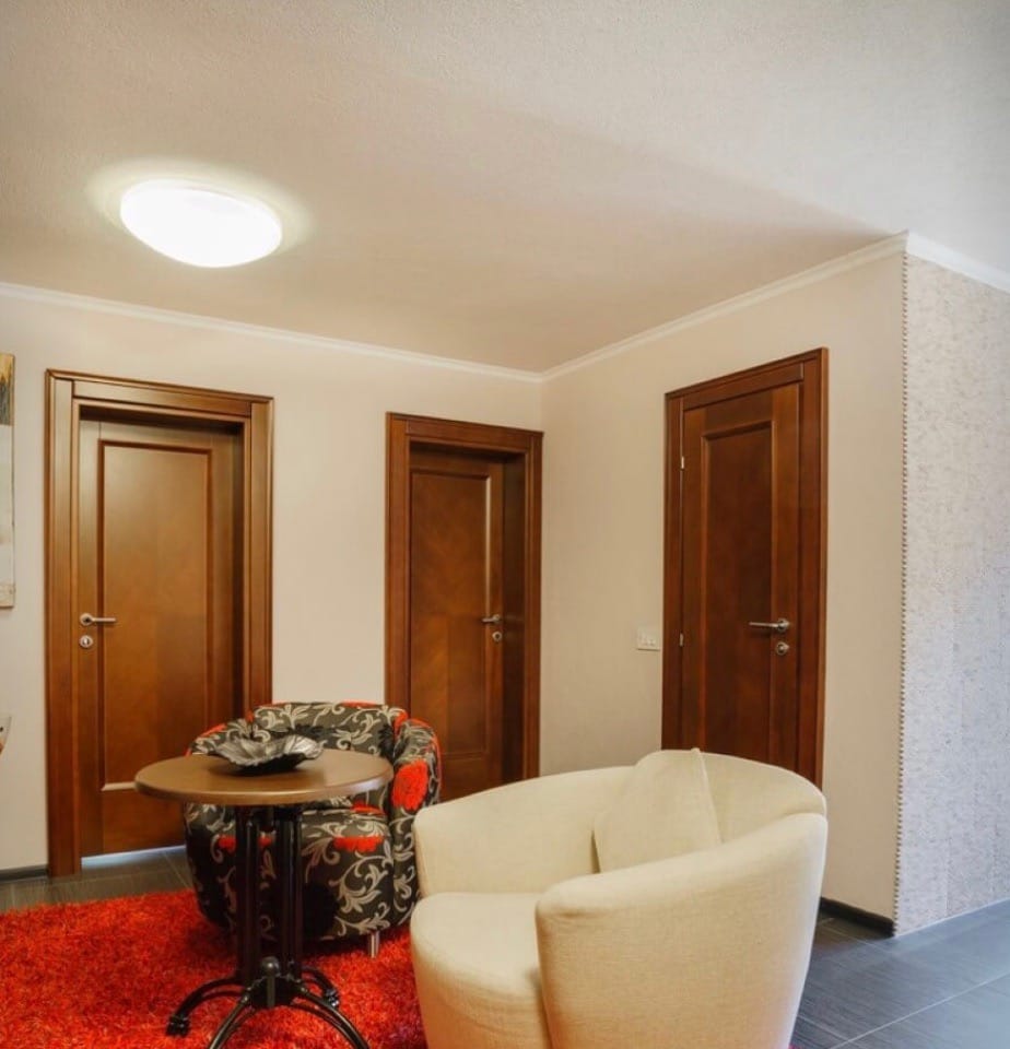 Enterijer dnevne sobe u vili u Stolivu, Crna Gora: svetli zidovi, drvena vrata, fotelje i crveni tepih.