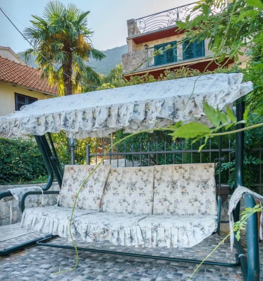 Vrtna ljuljaška s cvetnim printom na terasi vile u Stolivu, Crna Gora, u pozadini planina i mediteranskog vrta.