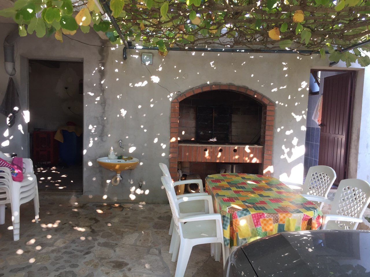 Taş barbekülü ve dinlenme alanlı уютlu teras, Kırımovitsa, Karadağ. Üzüm asmasıyla kaplı sundurma altında yazlık mutfak.
