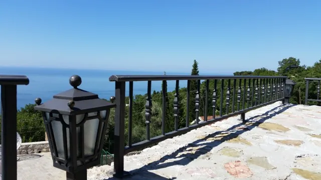 Widok z tarasu willi w Sutomore, Czarnogóra: kamienna podłoga, kute balustrady, latarnia uliczna i panoramiczny widok na morze.