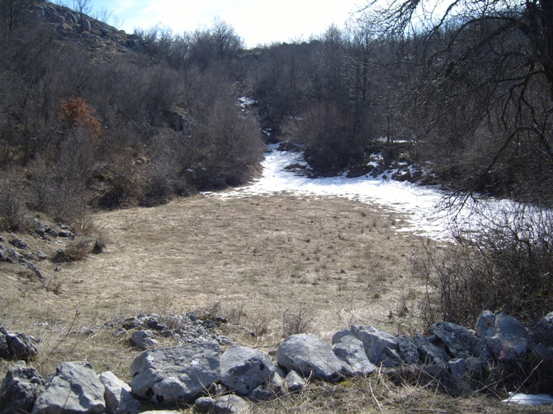 Land plot in the mountainous area of Cetinje, Montenegro: view of rocky soil, dry grass, and remnants of snow.