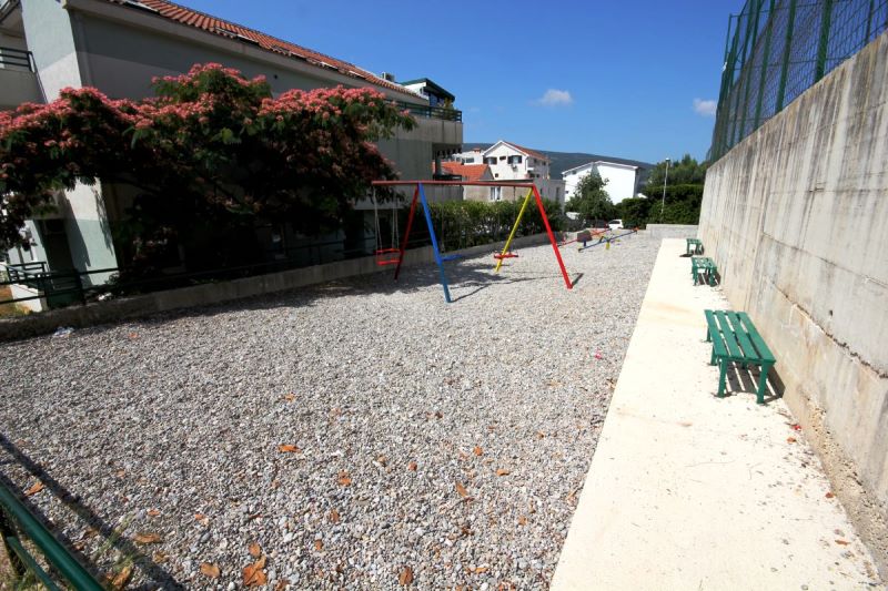 Aire de jeux avec balançoires et bancs près d’un immeuble résidentiel à Đenovići, Monténégro, vue sur la cour de l’immeuble.