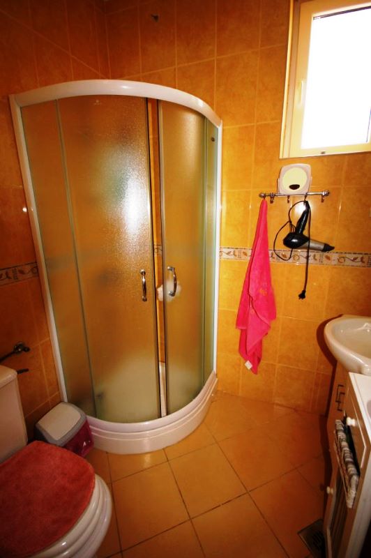 Salle de bain avec cabine de douche dans une maison, Genovici, Monténégro : carrelage aux tons chauds, sanitaires et fenêtre.