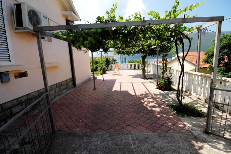 Terrasse de la maison à Đenovići, Monténégro : terrasse pavée avec une pergola de vigne et vue sur la mer et les montagnes.