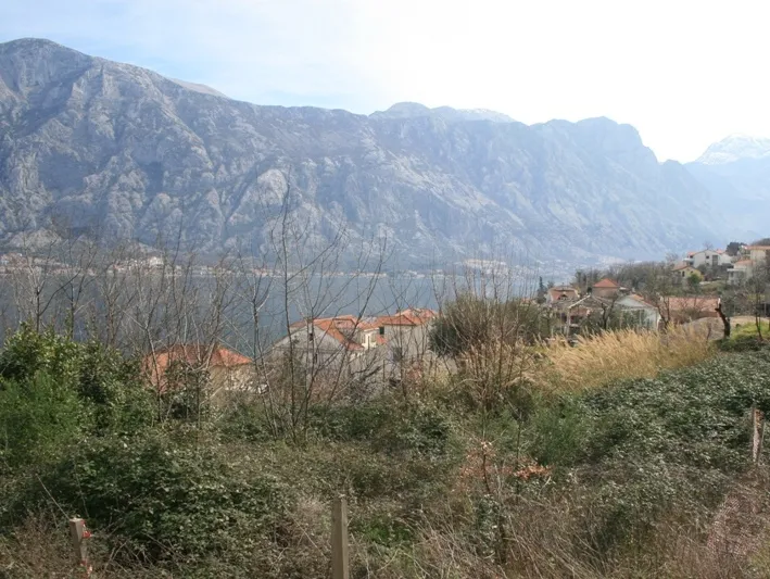 Çalıların ve ev çatılarının arkasında dağ ve deniz manzarası