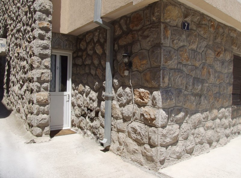 Eingang zum Hotel in Bečići, Montenegro: Fassade des Gebäudes mit Verkleidung aus Naturstein und weißer Kunststofftür.
