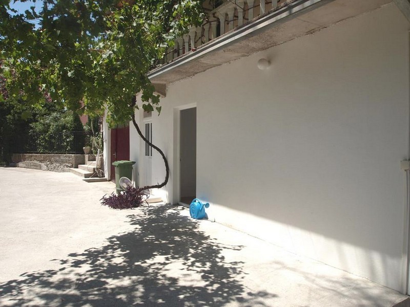 Weiße Fassade eines Hotels in Bečići, Montenegro, mit Terrasse, Weinrebe und Eingang zum Zimmer im Erdgeschoss.