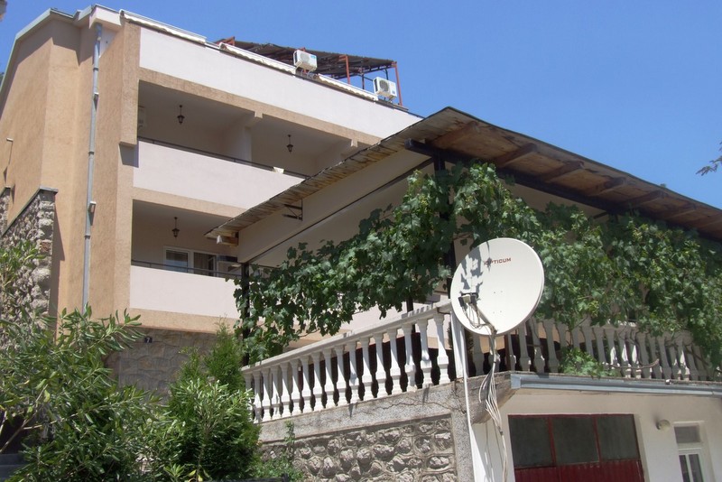 Dreistöckiges Hotel in Bečići, Montenegro: Fassade mit Balkonen, Terrasse mit Weinreben und Steinsockelverkleidung.