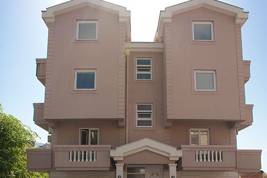 Fassade eines dreistöckigen beigen Hotels mit Balkonen und Panoramafenstern in Bečići, Montenegro.