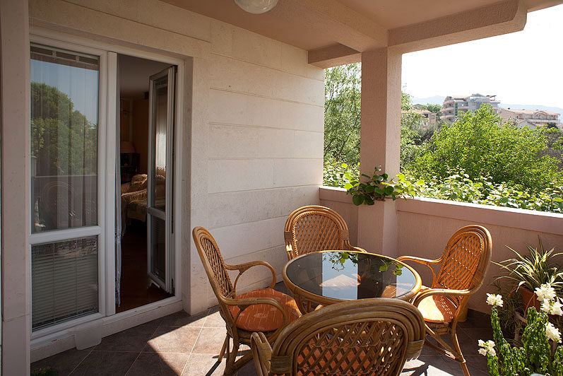 Gemütlicher Balkon mit Rattanmöbeln und Blick ins Grüne im Hotel in Bečići, Montenegro. Terrasse mit rundem Tisch und Stühlen.