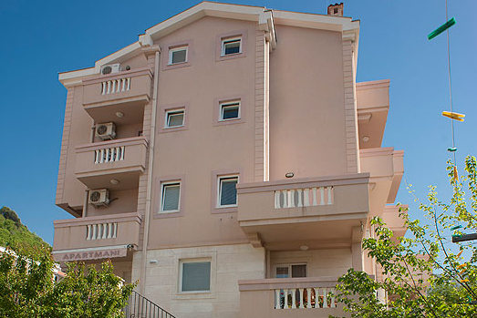 Fassade eines vierstöckigen Hotels in Bečići, Montenegro, mit Balkonen, Klimaanlagen und heller Steinverkleidung.