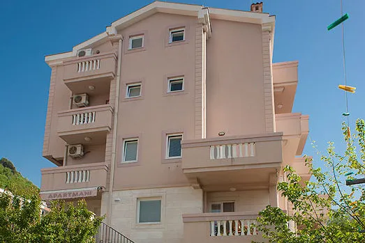Fasada czteropiętrowego hotelu w Bečići, Czarnogóra, z balkonami, klimatyzatorami i wykończeniem z jasnego kamienia.