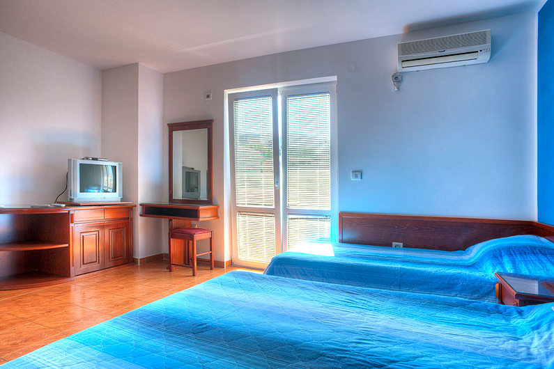 Schlafzimmer im Hotel in Bečići, Montenegro: zwei Betten, Holzmöbel, Schminktisch mit Spiegel und Klimaanlage.