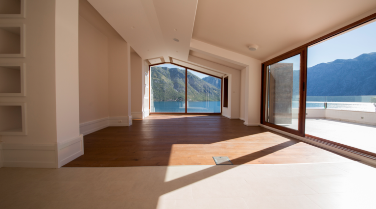 Geräumiges Wohnzimmer mit Panoramablick auf die Bucht von Kotor, Montenegro, Holzboden und Zugang zur Terrasse.