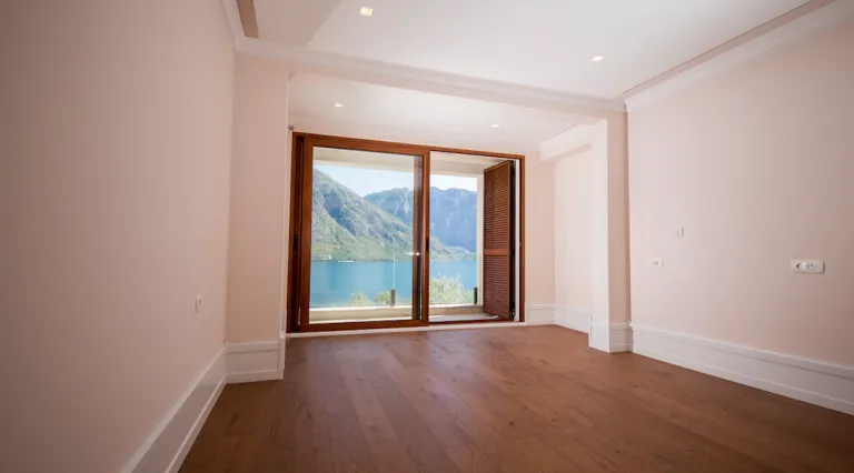 Leeres Zimmer mit Holzboden und großer Balkontür.