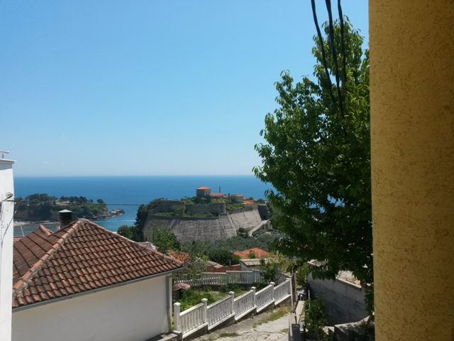 Pogled sa balkona kuće u Ulcinju, Crna Gora: panorama na staru tvrđavu, more i krovove grada sa crepovima.