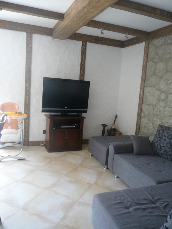 Wohnzimmer in einer Villa in Bigovo, Montenegro: Innenraum mit Holzbalken, Steinwand, Sofa und TV-Bereich.