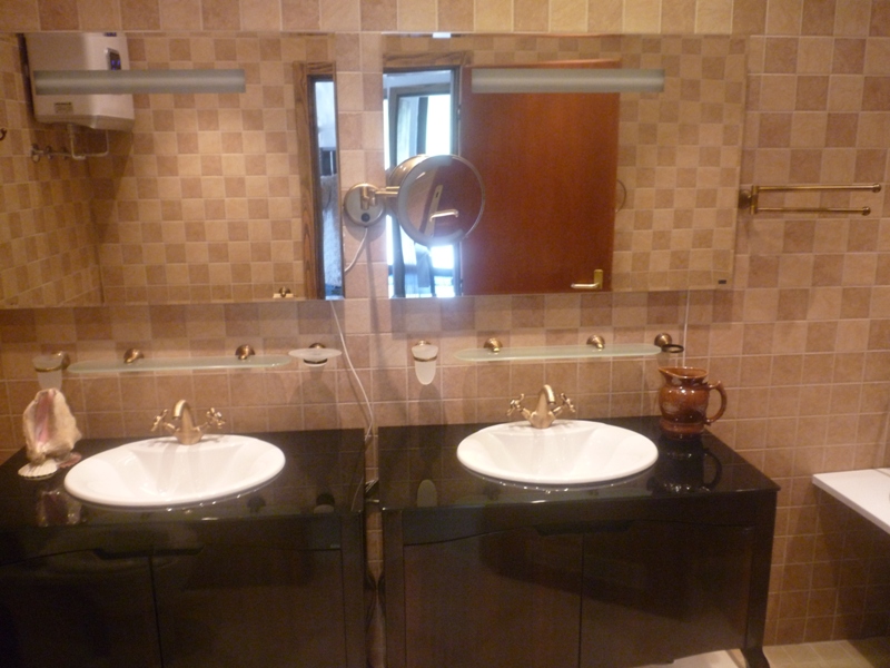 Badezimmer mit zwei Waschbecken und schwarzem Unterschrank in einer Villa in Bigovo, Montenegro. Verkleidet mit beigen Fliesen.