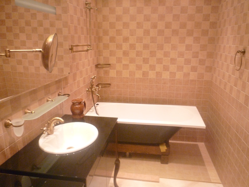 Badezimmer in einer Villa in Bigovo, Montenegro: beige Fliesen, klassische Badewanne und Waschbecken mit Messingarmaturen.