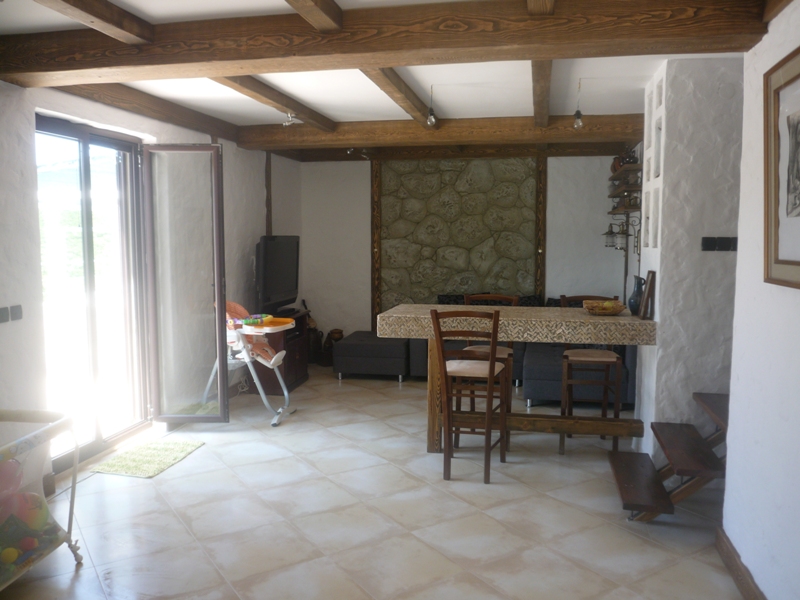 Wohnzimmer mit Steinwand und Holzbalken in einer Villa in Bigovo, Montenegro: Essbereich und Ausgang zur Terrasse.
