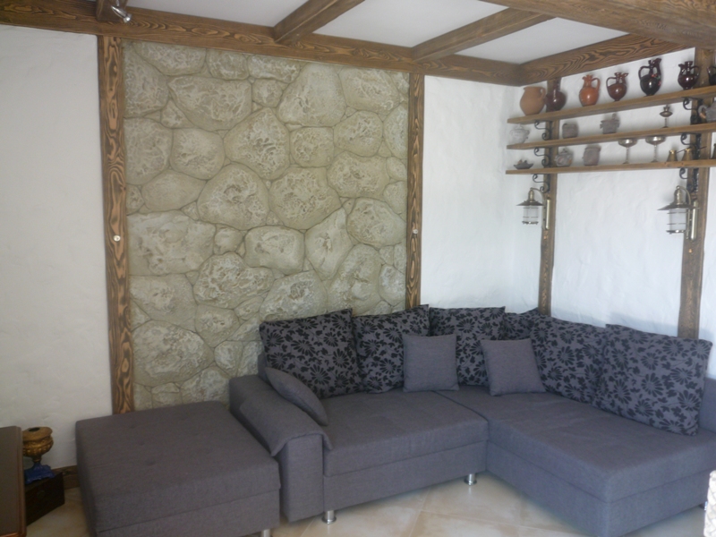 Wohnzimmer in einer Villa in Bigovo, Montenegro: Ecksofa, Wandverkleidung aus Naturstein und Holzbalken.