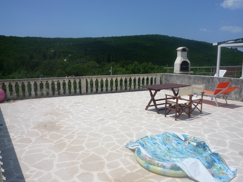 Terrasse der Villa in Bigovo, Montenegro: Steinboden, Gartenmöbel, Grill und Panoramablick auf grüne Berge.