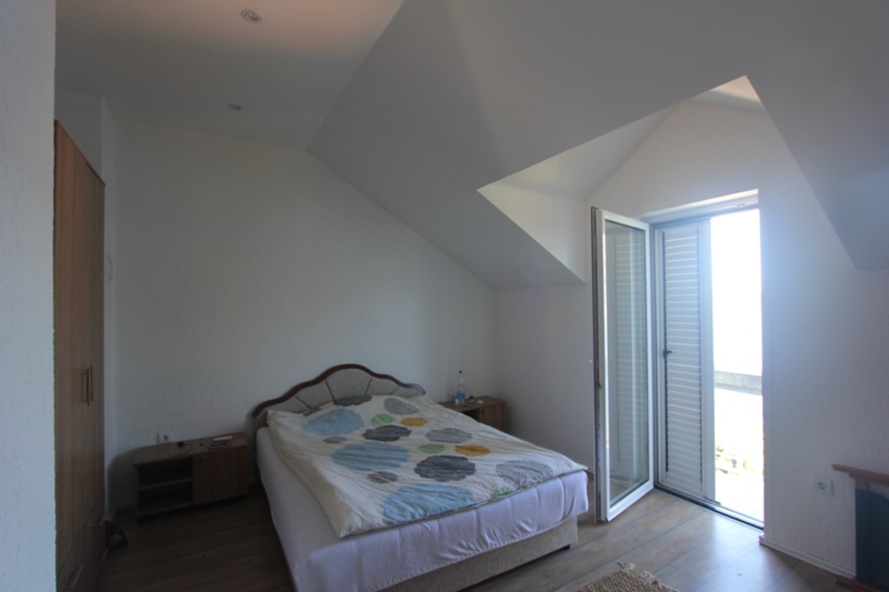 Schlafzimmer im Dachgeschoss eines Hauses in Luštica, Montenegro: Doppelbett, Holzschrank und Zugang zum Balkon.