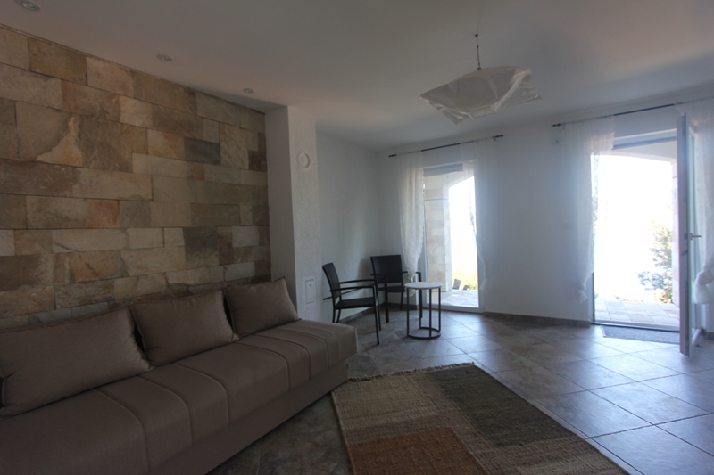 Wohnzimmer in einem Haus in Luštica, Montenegro: Steinverkleidung an der Wand, ein weiches Sofa und Zugang zur Terrasse mit Meerblick.