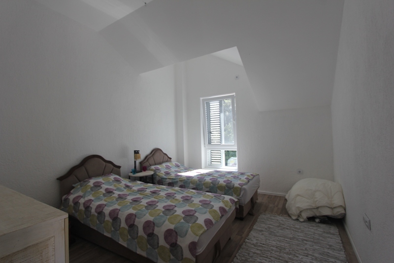 Helles Schlafzimmer mit zwei Betten in einem Haus auf der Halbinsel Luštica, Montenegro: Dachschräge und Blick aus dem Fenster.