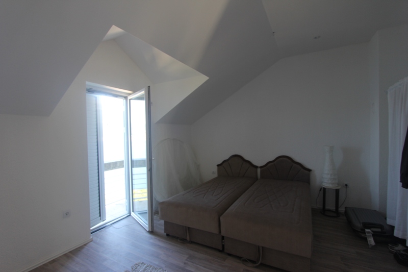 Schlafzimmer im Dachgeschoss eines Hauses in Luštica, Montenegro: zwei Betten, helle Ausstattung und Zugang zum Balkon mit Aussicht.