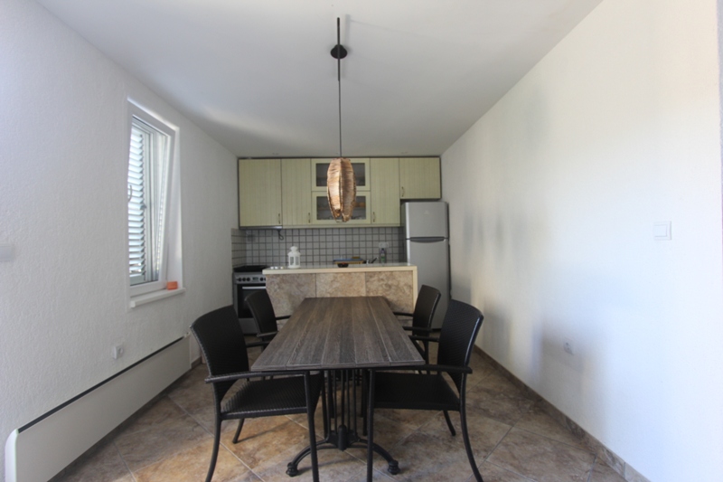 Küche mit Essbereich in einem Haus in Luštica, Montenegro: Essbereich mit dunklem Tisch, hellem Küchenmöbel und Fliesenboden.