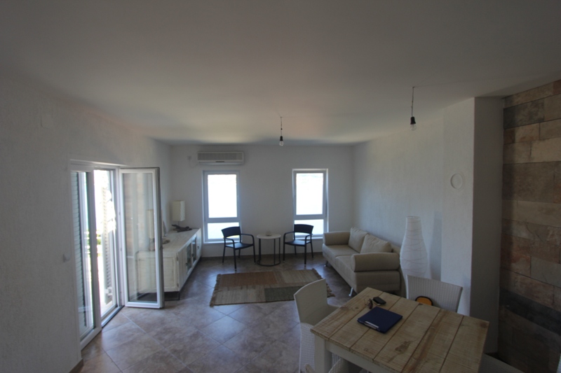 Helles Wohnzimmer mit Steinverkleidung in einem Haus in Luštica, Montenegro: ein weiches Sofa, ein Essbereich und Zugang zur Terrasse.