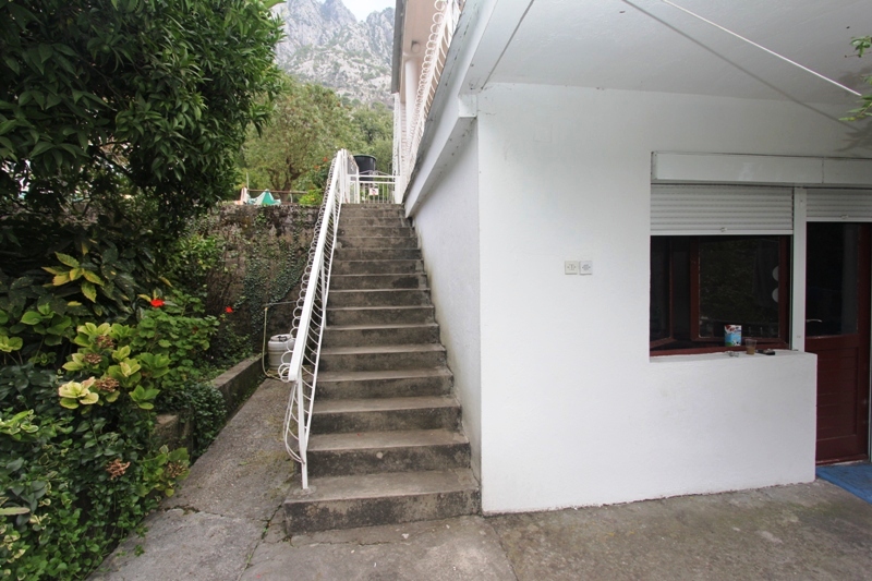 Betonsko stepenište kod ulaza u stan u Dobroti, Crna Gora, s pogledom na planine i zelenu baštu uz kuću.