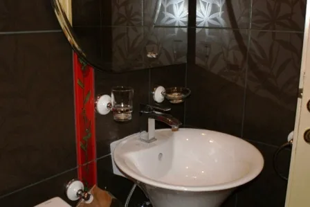 Badezimmer in einem Haus in Igalo, Montenegro: weißes Waschbecken, dunkle Fliesen mit Pflanzenmuster und Spiegel.