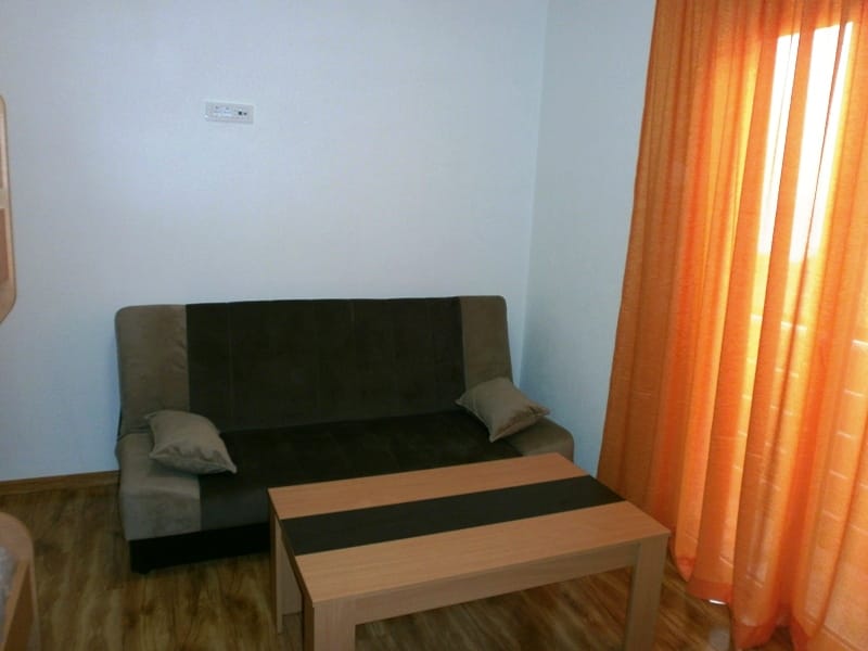 Living room in the Shushan mini-hotel, Montenegro: a brown sofa, coffee table, and bright orange curtains in the interior.