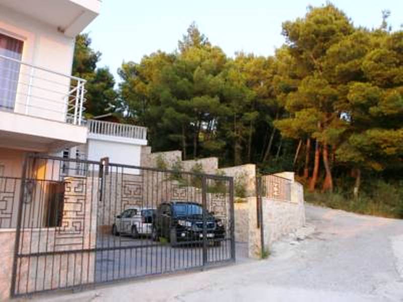 Facade of a mini-hotel in Shushan, Montenegro: private parking behind wrought-iron gates and a view of the coniferous forest next to the house.