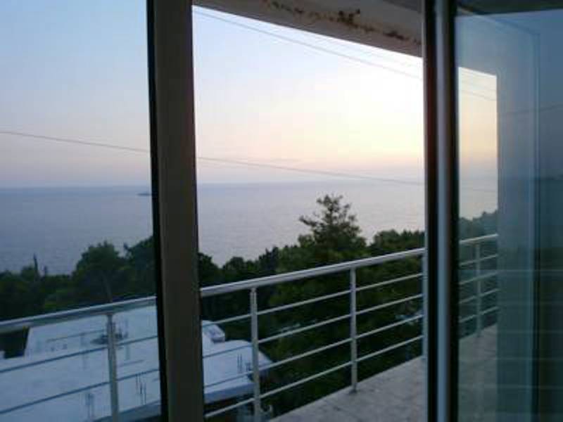 View from the balcony of a mini-hotel in Shushan, Montenegro: a panorama of the Adriatic Sea, green trees, and a terrace at sunset.