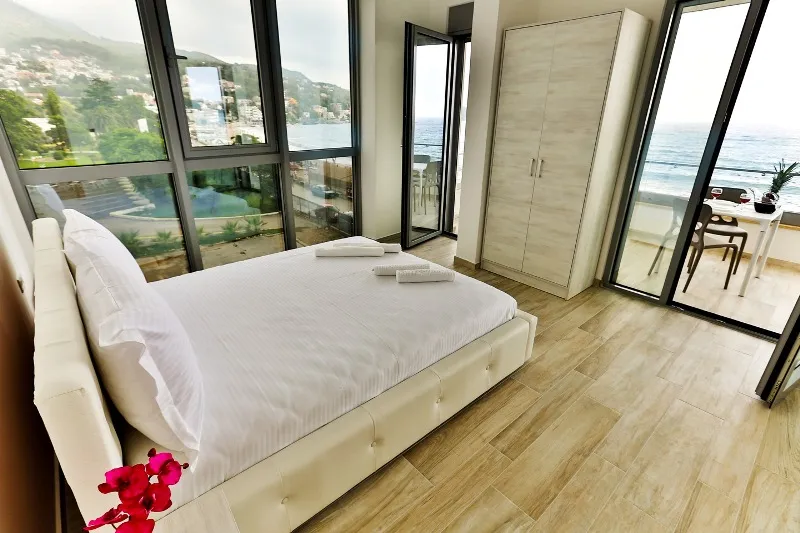 Schlafzimmer in einer Wohnung in Dobri Vody, Montenegro: Doppelbett, Panoramafenster mit Meerblick und Terrasse.