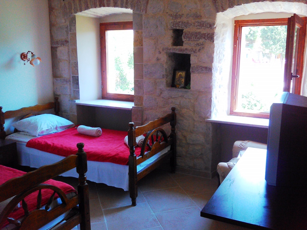 Schlafzimmer in einem Haus in Mišići, Bar, Montenegro: zwei Betten, Steinwände, Bogenfenster und Blick auf den Garten.