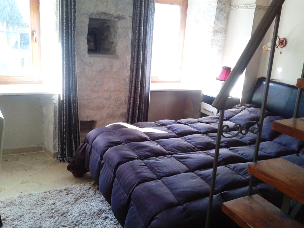 Schlafzimmer in einem Haus in Mišići, Bar, Montenegro: Steinwände, Doppelbett, Holztreppe und Blick aus dem Fenster.