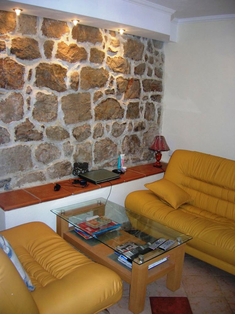 Wohnzimmer in einem Haus in Mišići, Bar, Montenegro: gelbe Ledersofas, Glastisch und Akzentwand aus Stein.