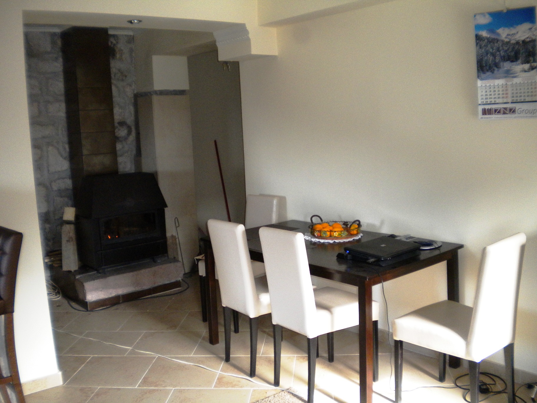 Wohnzimmer mit Kamin und Essbereich in einem Haus in Mišići, Bar, Montenegro: dunkler Tisch, weiße Stühle und Steinverkleidung.