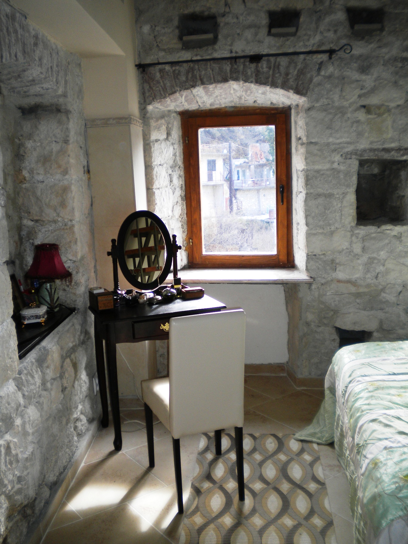 Schlafzimmer in einem Steinhaus in Mišići, Bar, Montenegro: Schminktisch mit Spiegel und Blick aus dem Fenster auf die Stadt.