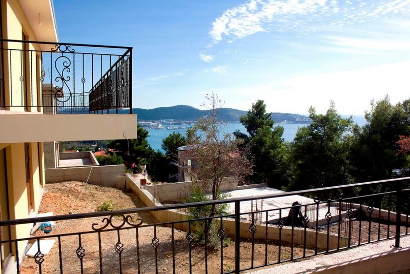 Blick vom Balkon eines Hauses in Šušanj, Montenegro: schmiedeeisernes Geländer, Panoramablick auf das Meer, die Berge und ein Baugrundstück.