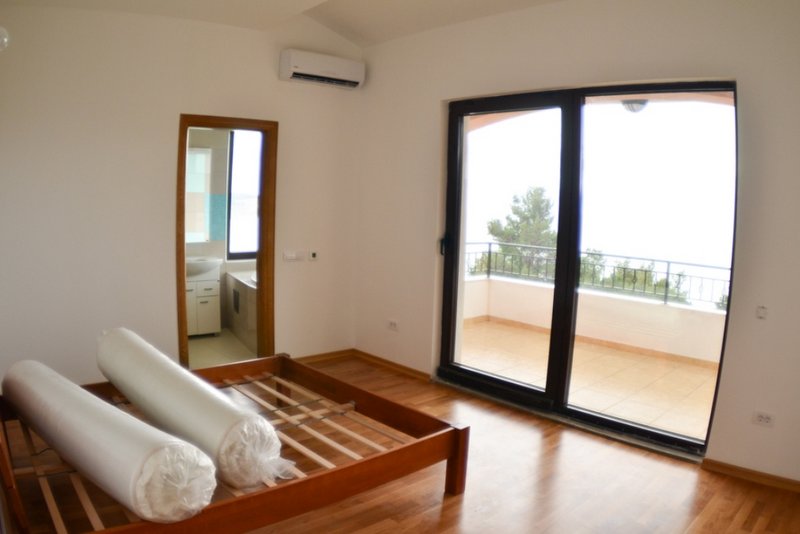 Schlafzimmer in einem Haus in Shushan, Montenegro: Holzbett, Zugang zur Terrasse mit Aussicht und separates Badezimmer.