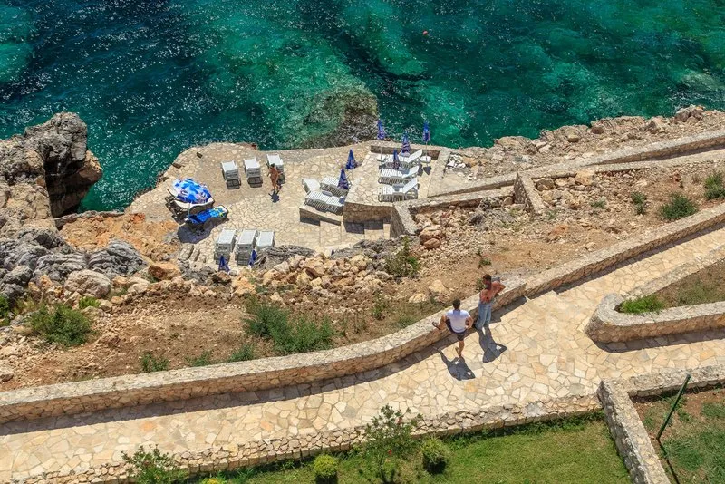 Blick von oben auf einen Privatstrand mit Liegestühlen und das azurblaue Meer an einer Wohnanlage in Dobra Voda, Montenegro.